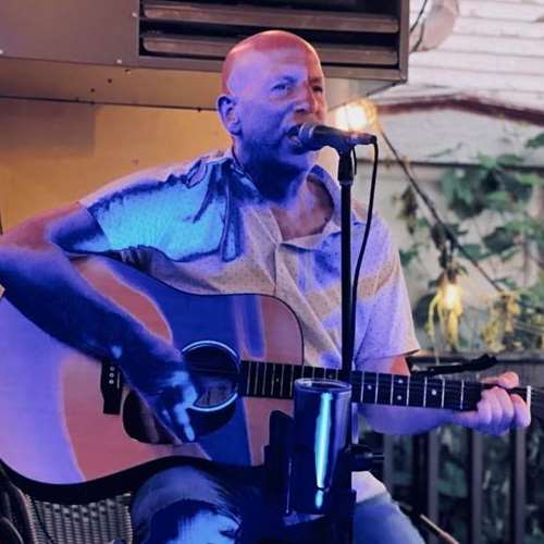 Man sitting on stool singing into a microphone and playing the guitar