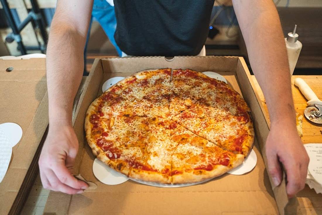 Large cheese pizza going into a takeout box